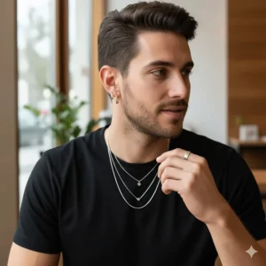A styled photo of a man wearing a black shirt, showcasing a pair of simple gold hoop earrings layered with other jewelry.