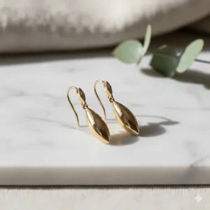 A pair of elegant 14k gold drop earrings displayed on a minimalist white marble background.