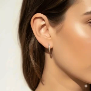 Model wearing small gold diamond huggie earrings in the first lobe piercing.