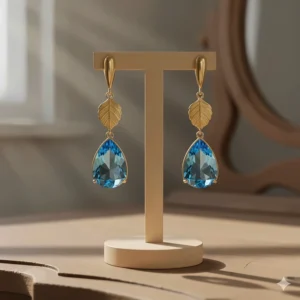 Elegant dangling gold gemstone earrings with pear-cut blue topaz stones and gold leaf details.