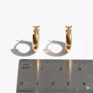 A pair of small and classic 10 karat gold hoop earrings next to a ruler showing the perfect petite size.