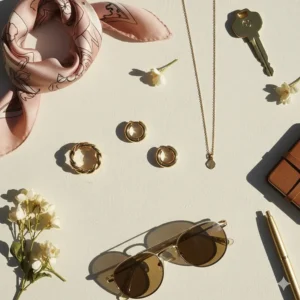 Aesthetic jewelry flatlay featuring small gold hoop earrings, a gold ring, and a silk scarf.