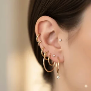 Multiple ear piercings featuring thin gold hoops layered with tiny gold studs.