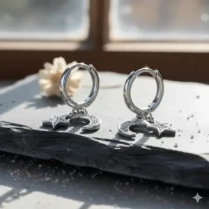 Close-up of celestial-themed silver huggie earrings featuring dangling star and crescent moon charms.