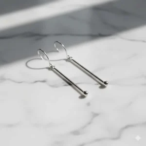 Pair of minimalist sterling silver long dangle earrings on a white marble surface.