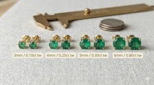 A size comparison chart showing different carat weights for gold emerald stud earrings.