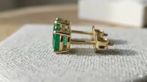 Side view of emerald stud earrings showing the secure gold basket setting and post.