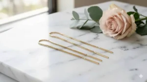 Minimalist gold box chain threader earrings displayed on a white marble surface.