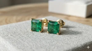 Princess-cut emerald stud earrings handcrafted in a yellow gold four-prong mount.
