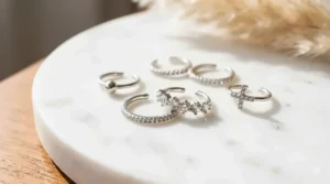 Minimalist silver ear cuffs with clear crystals displayed on a white marble surface.