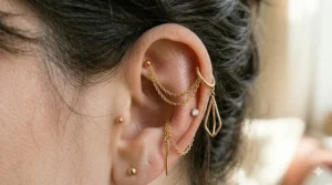 A trendy helix earring featuring a delicate gold chain connecting a stud to the lobe piercing.